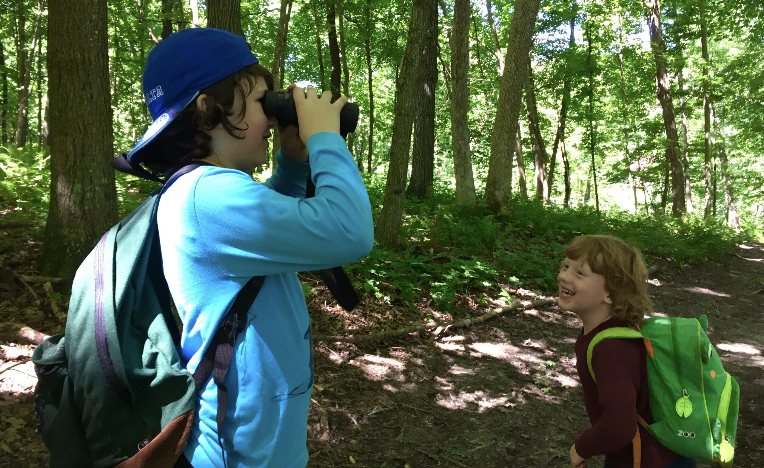 a boy looks on with binoculars while another smiles
